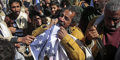 ARCHIV - Ein Anhänger der jemenitischen Huthi-Bewegung zerreißt während eines Protest vor der geschlossenen US-Botschaft eine US-Fahne, nachdem US-Außenminister Pompeo angekündigt hat, die Huthi-Rebellen als Terrororganisation einzustufen. Foto: H...