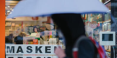 Eine Passantin geht mit einem Regenschirm am Schaufenster einer Apotheke vorbei, in dem auf vorrätige Masken hinweisen wird. Foto: Ole Spata/dpa