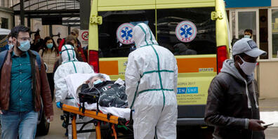 Medizinische Mitarbeiter in Schutzausrüstung transportieren einen Patienten auf einer Trage, um ihn in einem Krankenhaus in Athen zu verlegen. Foto: Marios Lolos/Xinhua/dpa