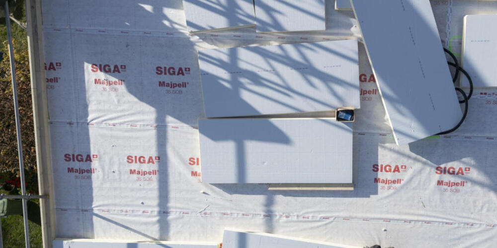 Bauarbeiter tragen und verteilen Isolierplatten auf dem Dach: Die Modernisierung der Dachdämmung trägt zur energetischen Sanierung eines Gebäudes bei und somit auch zur Reduktion von Treibhausgasen.