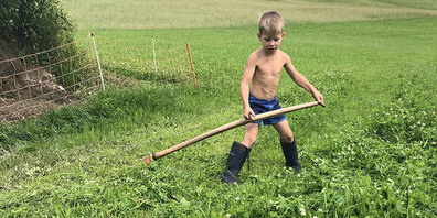 Im Sommer immer ohne T-Shirt, aber mit Gummistiefeln, übt der sechsjährige Raphael Kälin das Handmähen.