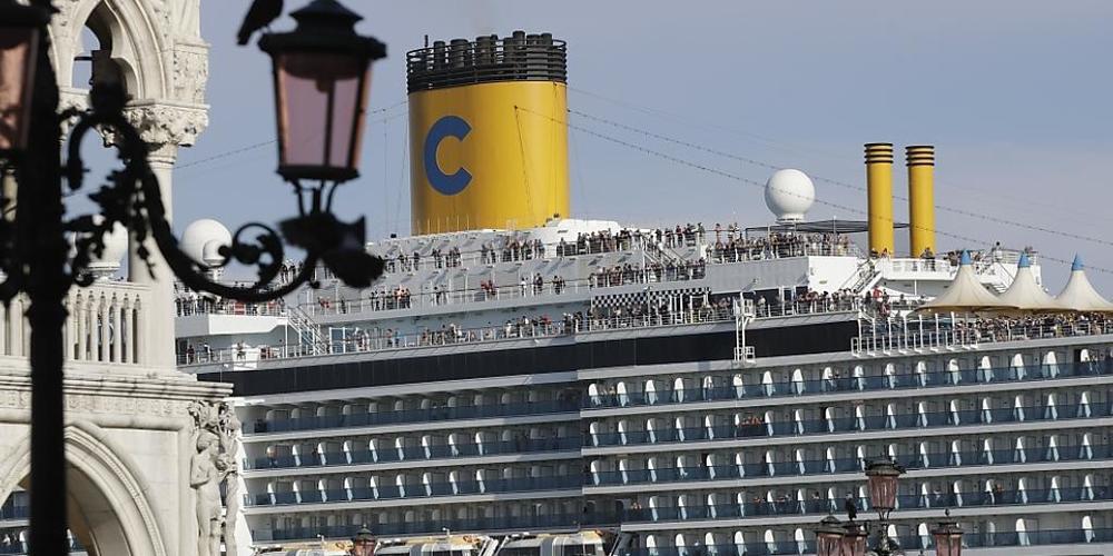 ARCHIV - Das Kreuzfahrtschiff «Costa Deliziosa» fährt am Markusplatz vorbei, auf dem zahlreiche Touristen unterwegs sind. Venedig will Kreuzfahrtschiffe nicht mehr so nahe an seinen historischen Stätten wie den Markusplatz ankern lassen. Foto: Luc...