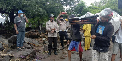 dpatopbilder - Menschen tragen einen Mann, der während einer Überschwemmung verletzt wurde. Foto: Ricko Wawo/AP/dpa
