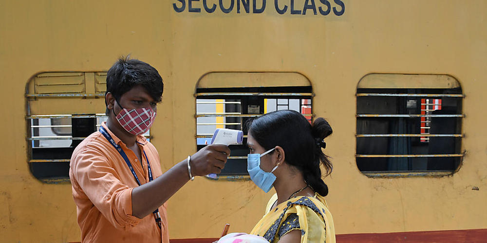 Ein Mitarbeiter misst die Temperatur bei einer Frau, die ein Baby auf dem Arm trägt, auf einem Bahnsteig im indischen Mumbai. Foto: Ashish Vaishnav/SOPA Images via ZUMA Wire/dpa