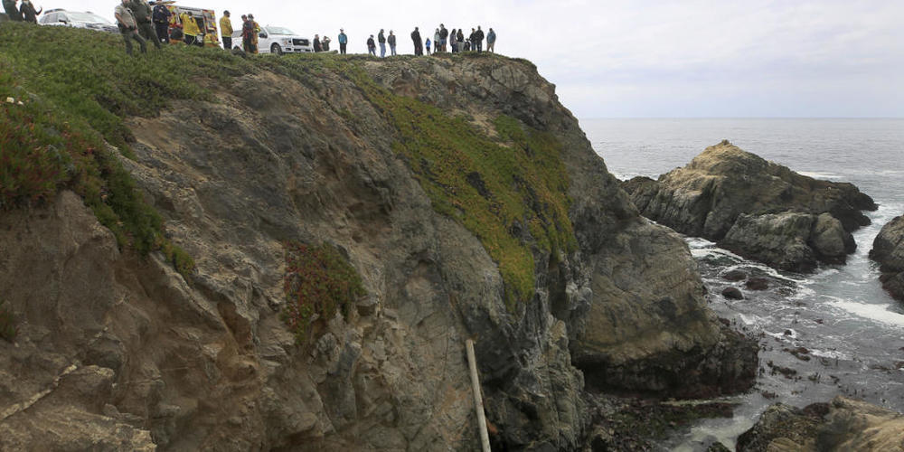 Das Wrack eines Autos liegt auf dem Dach nach einem Sturz von einer Klippe, während Feuerwehrleute die Unfallstelle sichern. Foto: Kent Porter/The Press Democrat/AP/dpa