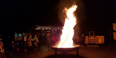 Alte Christbäume brennen, während Würste an der Feuerstelle grilliert werden.