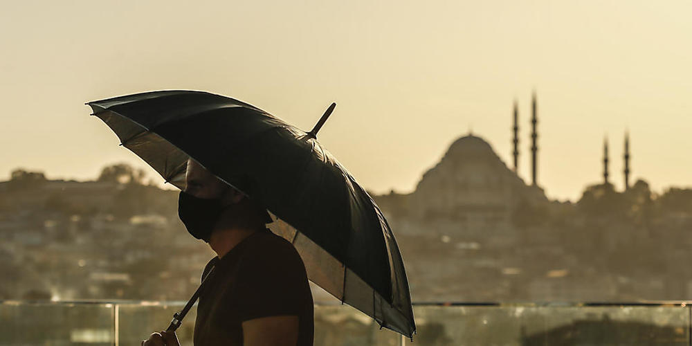 ARCHIV - Ein Tourist trägt einen Mund-Nasen-Schutz und hält einen Regenschirm während er von der Süleymaniye-Moschee über die Stadt blickt. (Archivbild) Foto: Emrah Gurel/AP/dpa